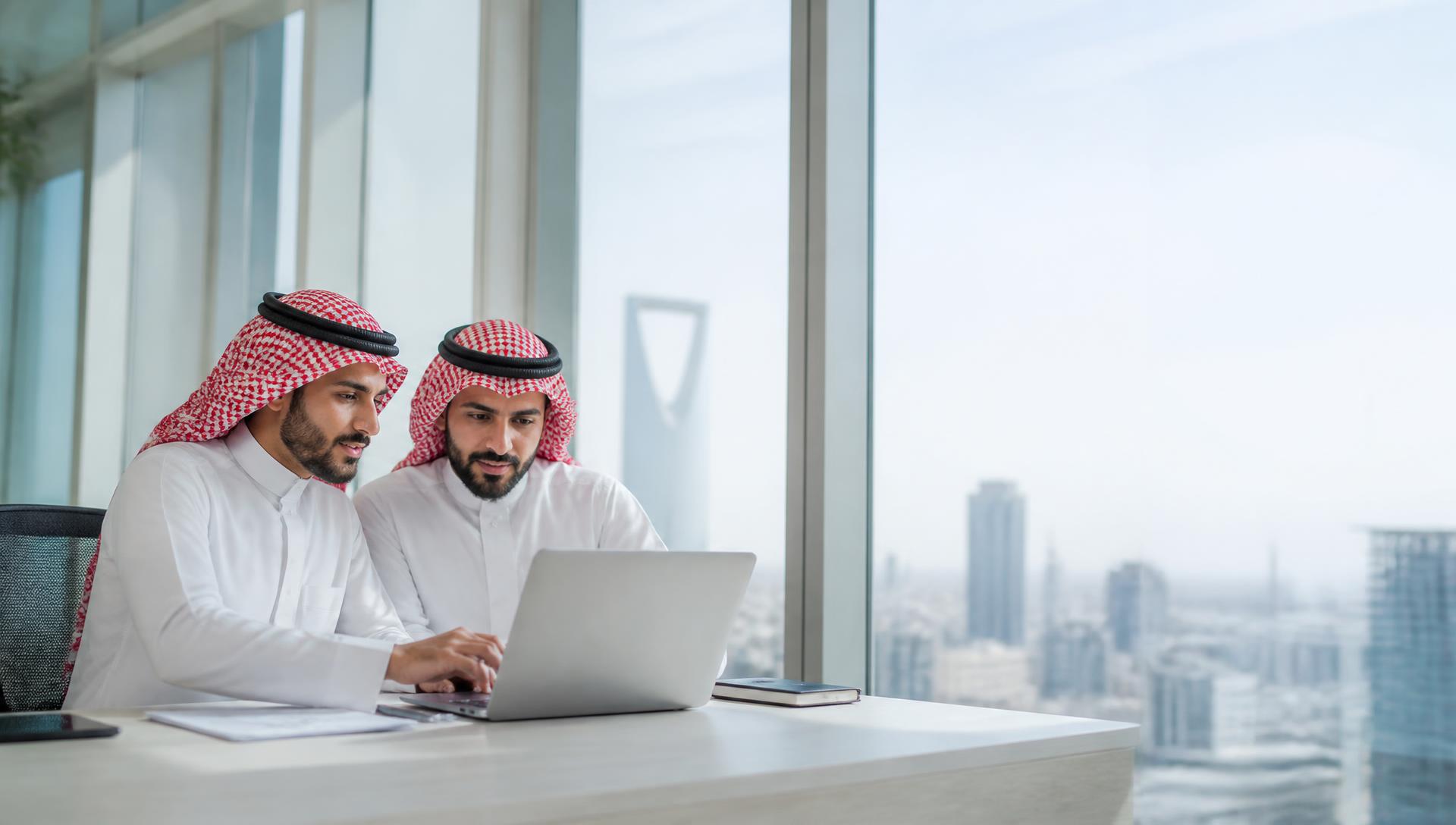 رجال أعمال سعوديون يعملون معًا على حاسب محمول في مكتب حديث بالرياض
